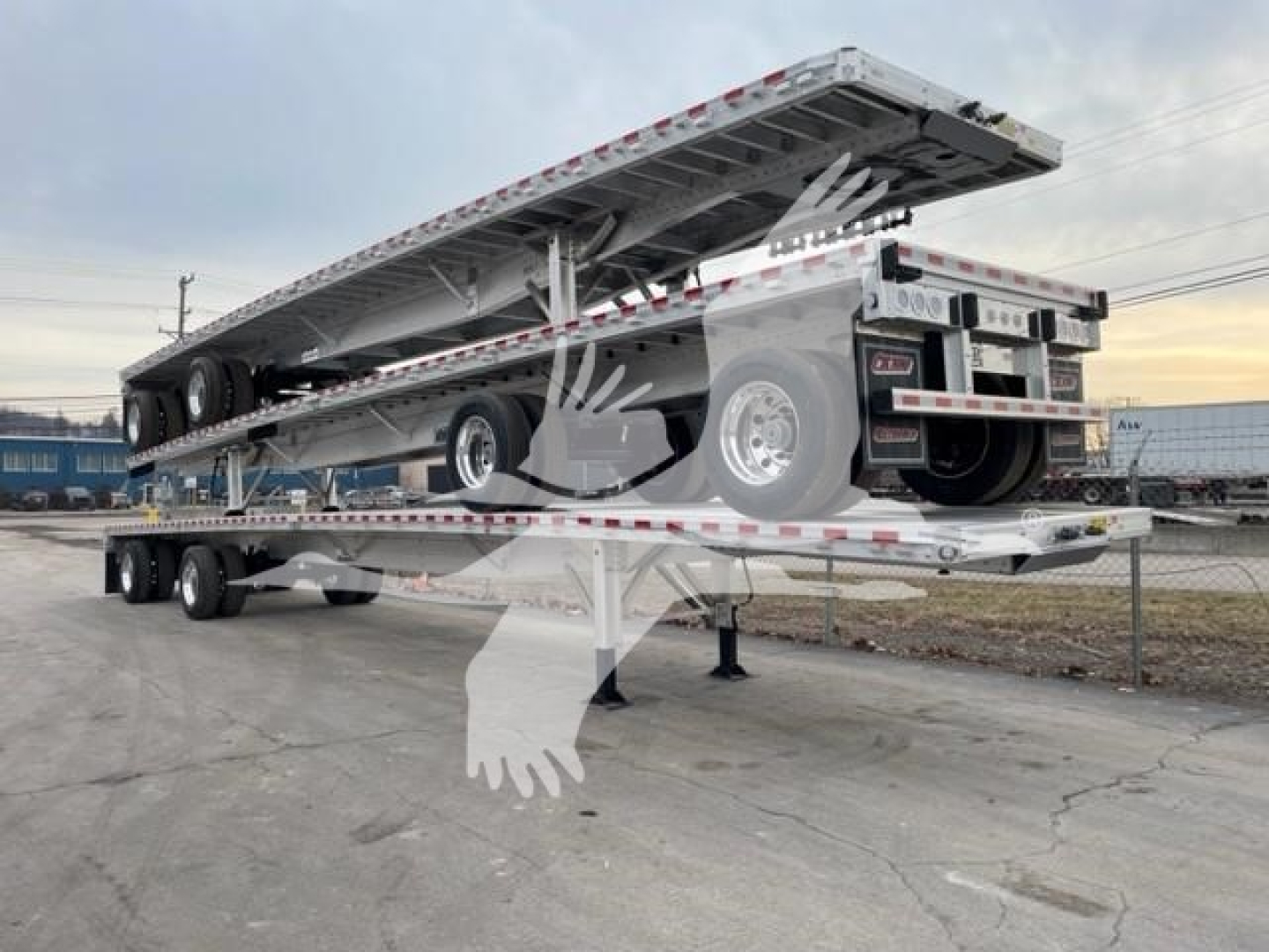 Flatbed trailer with an extended deck raised on a gooseneck, spare tire mounted on side, rear twin axles, reflective safety markings along edges.