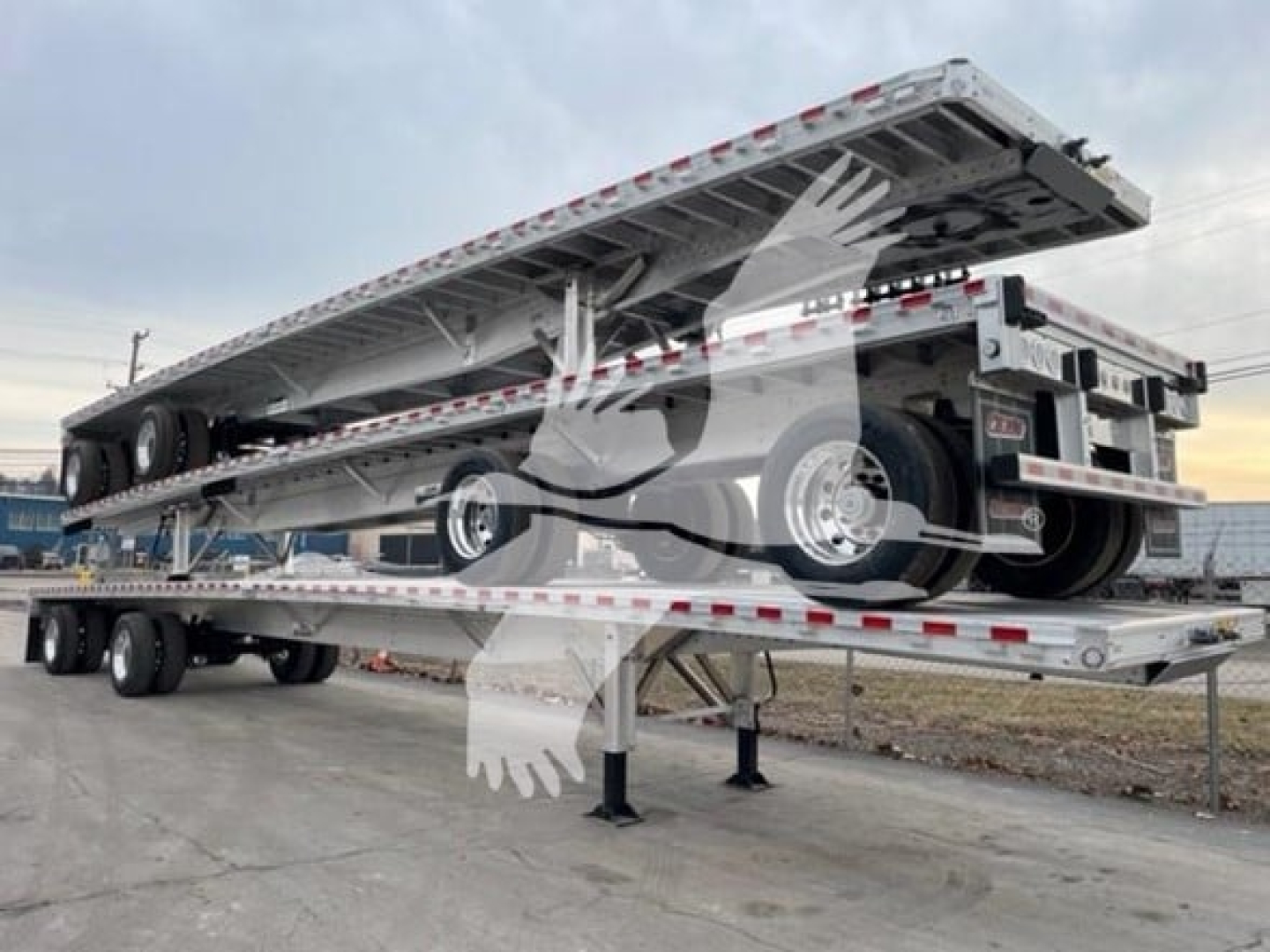 Flatbed trailer with multiple stacked deck sections showing undercarriage and wheels; tandem axle configuration visible.