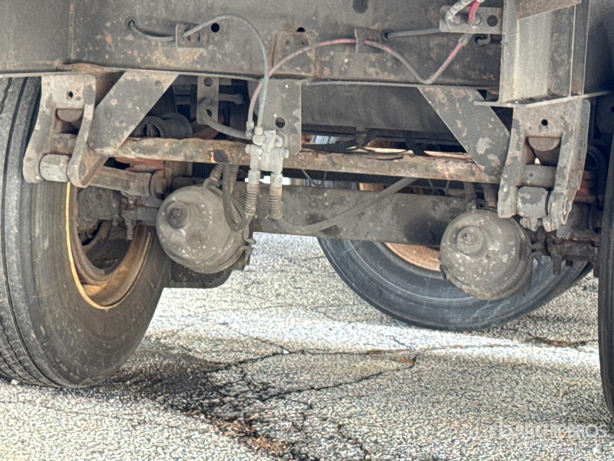 Trailer undercarriage showing axle, leaf springs, and wheels with mechanical components and hoses visible.