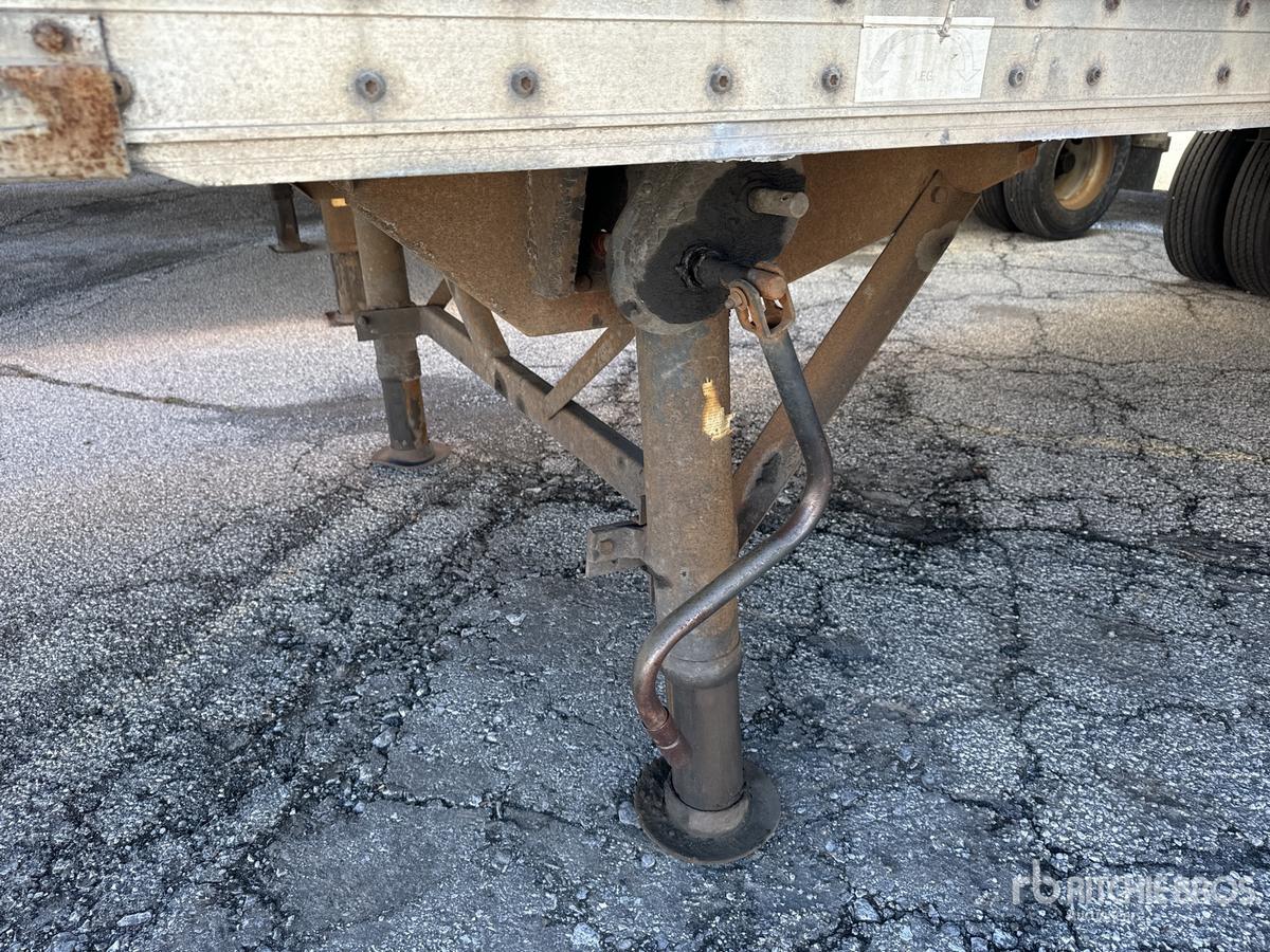 Trailer landing gear and undercarriage with crank jack and support leg, showing metal frame and wheel well. visible bolts and steel tubing.
