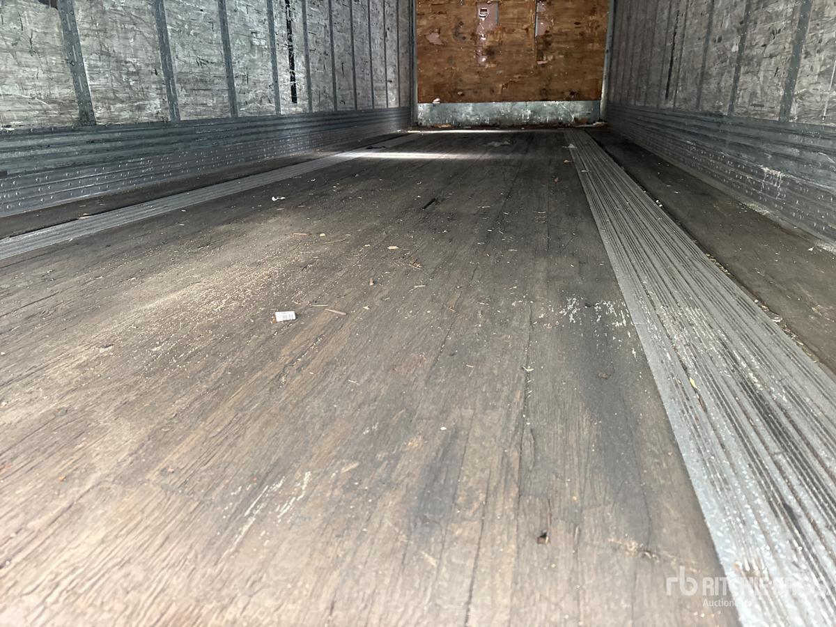 Trailer interior showing empty cargo area with wooden back wall and metal side walls; faint dirt and scuff marks on plywood floor; no visible markings.