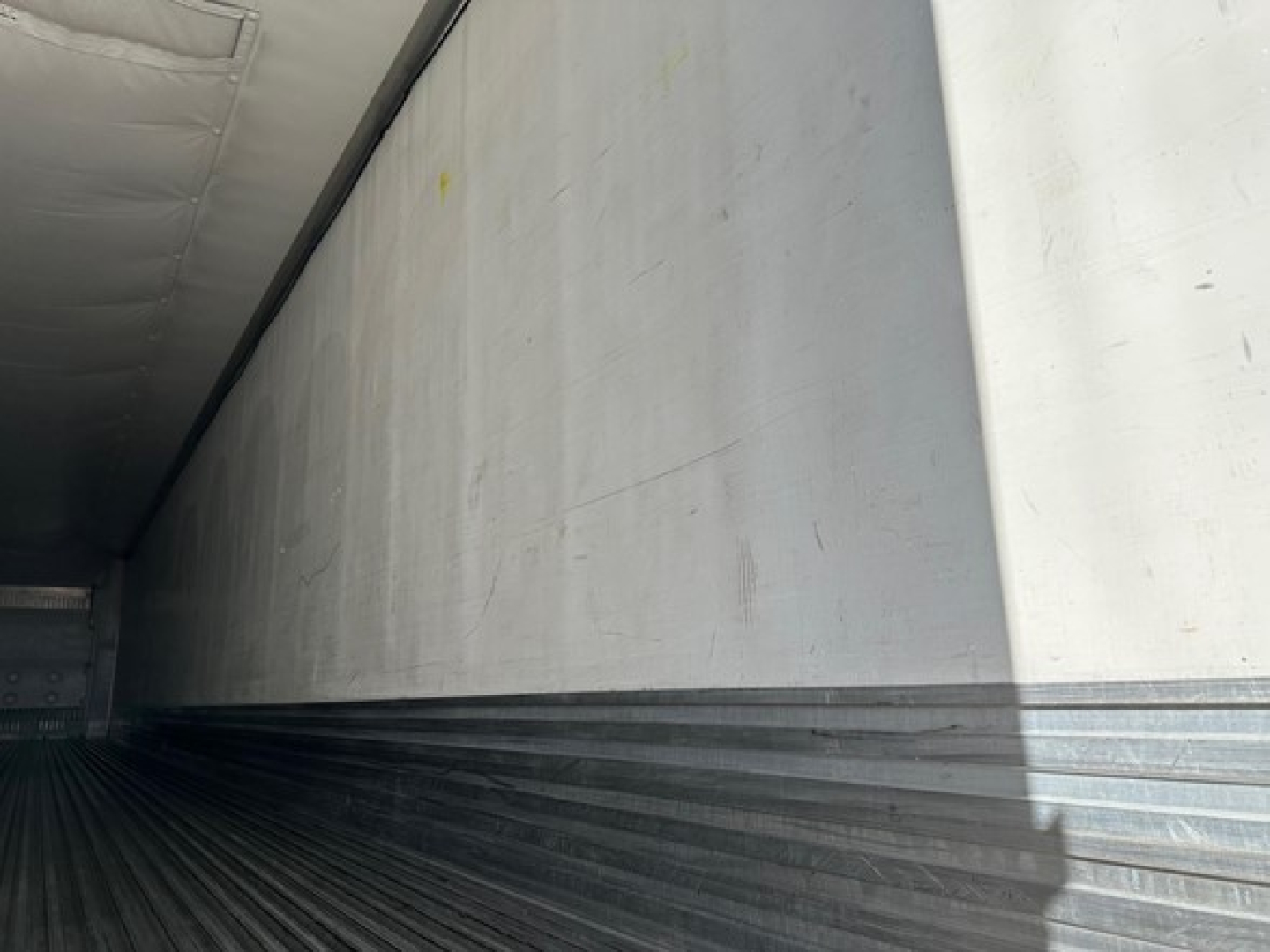 Interior of a utility trailer with metal walls and ribbed floor; faint yellow marks on side wall.