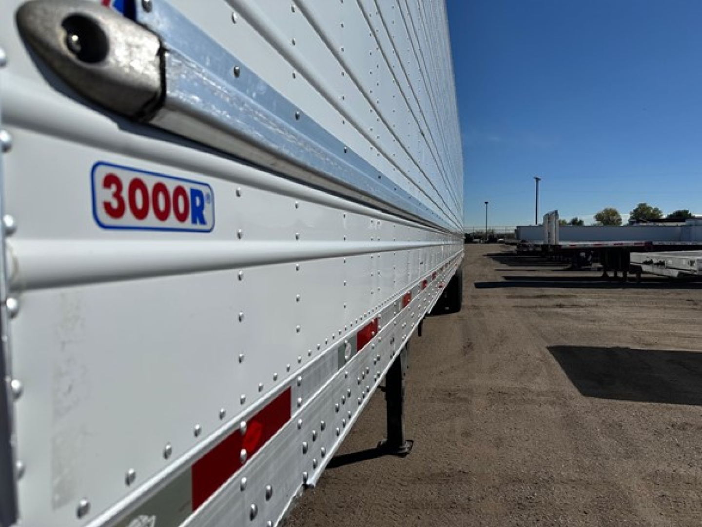 Trailer side panel with 3000R logo on white surface, riveted aluminum siding, red reflective tape, view along trailer length in a yard.