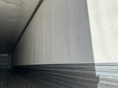 Interior of a utility trailer with metal walls and ribbed floor; faint yellow marks on side wall.