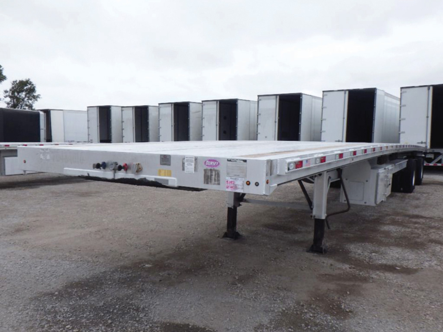 Flatbed trailer showing aluminum deck with landing gear and wheel wells in a lot.