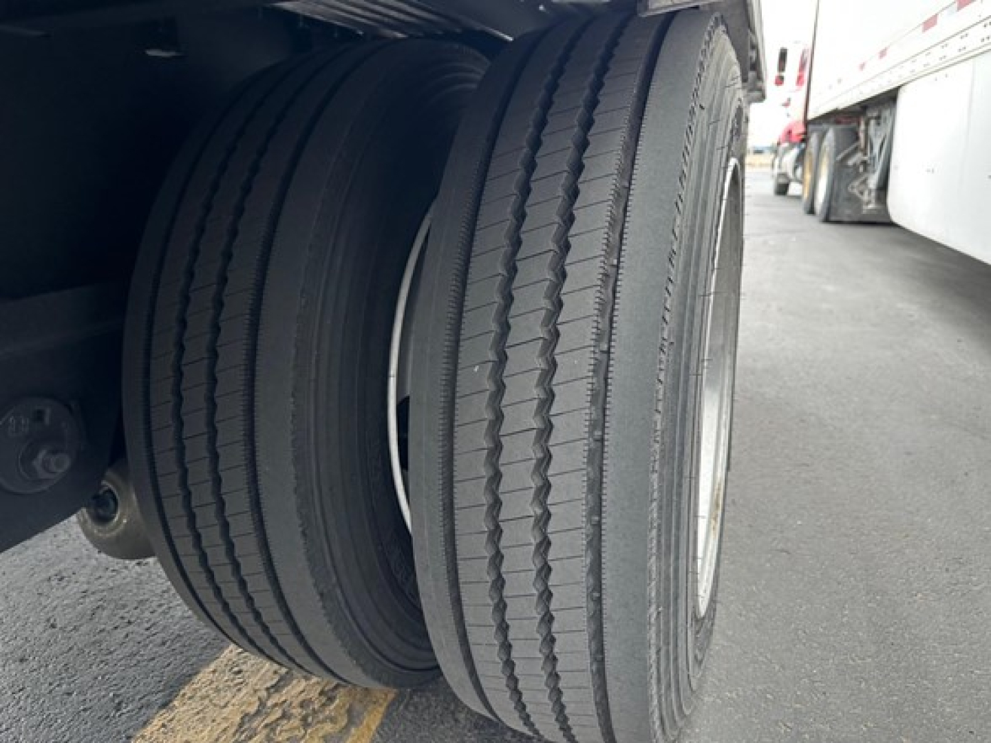 Dual rear trailer tires on a drop deck trailer with white cab visible in background.