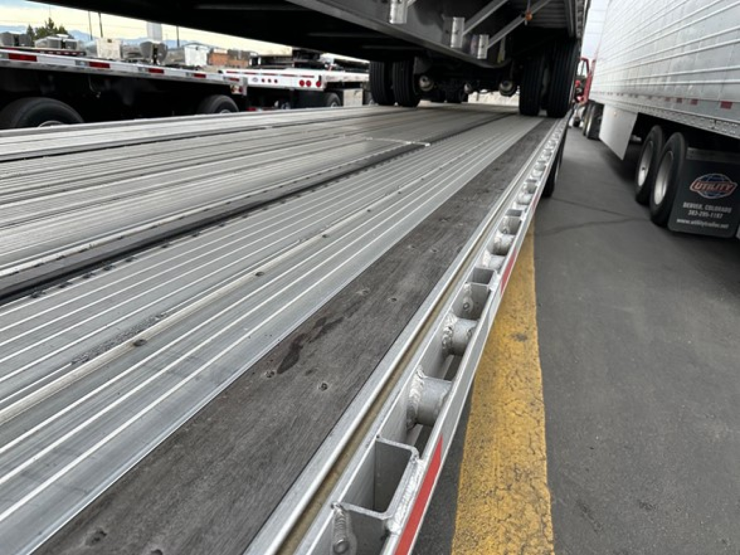 Trailer bed with metal drop deck surface and side rails showing a loading ramp area, utility trailer deck in a yard.
