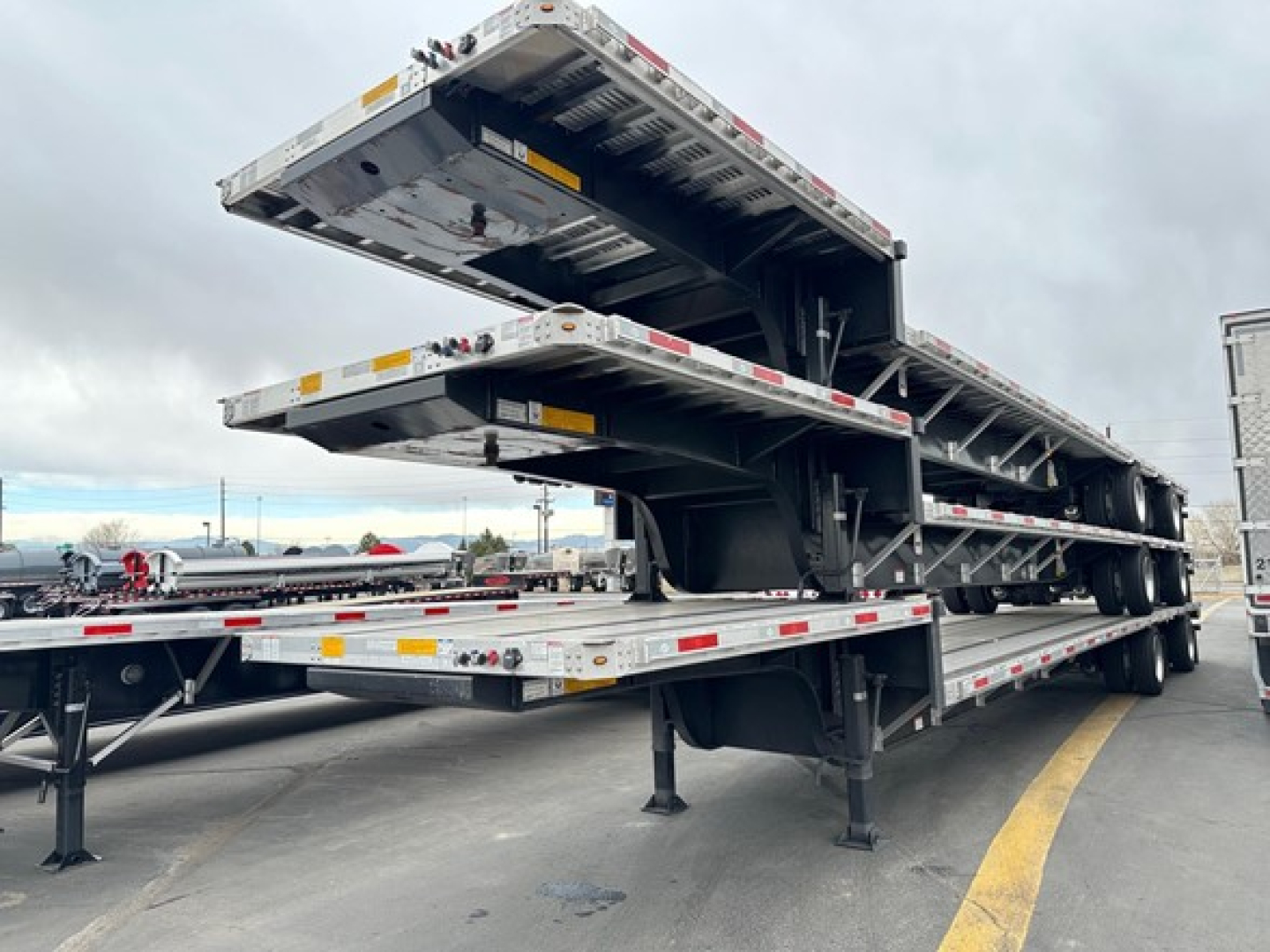Trailer deck showing stacked drop deck trailers with hydraulic tilting mechanism and supporting legs.