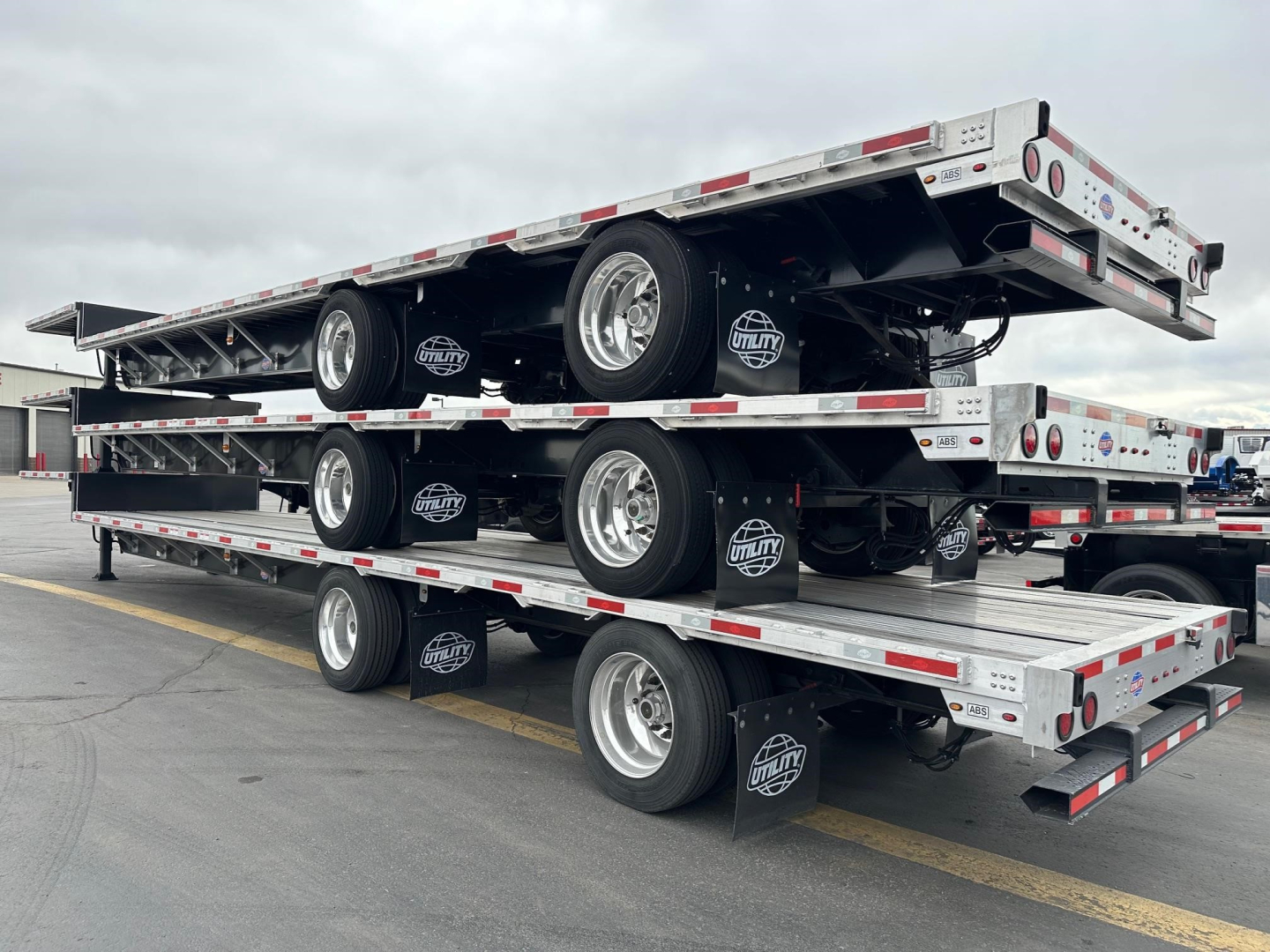 Stacked flatbed trailers on a multi-level trailer rack showing wheels, tires, and reflective safety rails.
