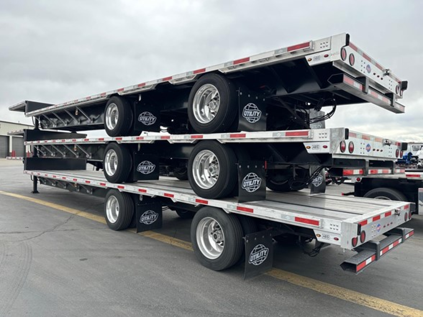Four stacked utility drop deck trailers with triple-axle configurations and white and red reflective tape.