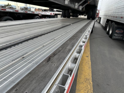 Trailer bed with metal drop deck surface and side rails showing a loading ramp area, utility trailer deck in a yard.