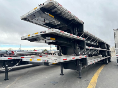 Trailer deck showing stacked drop deck trailers with hydraulic tilting mechanism and supporting legs.