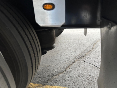 Trailer undercarriage showing a wheel, suspension, and frame with a small orange reflector and metal components.
