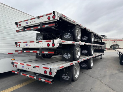 Multi-level utility trailer stack showing triple-deck drop deck trailers with metal sides, wheels, and Utility brand mud flaps.