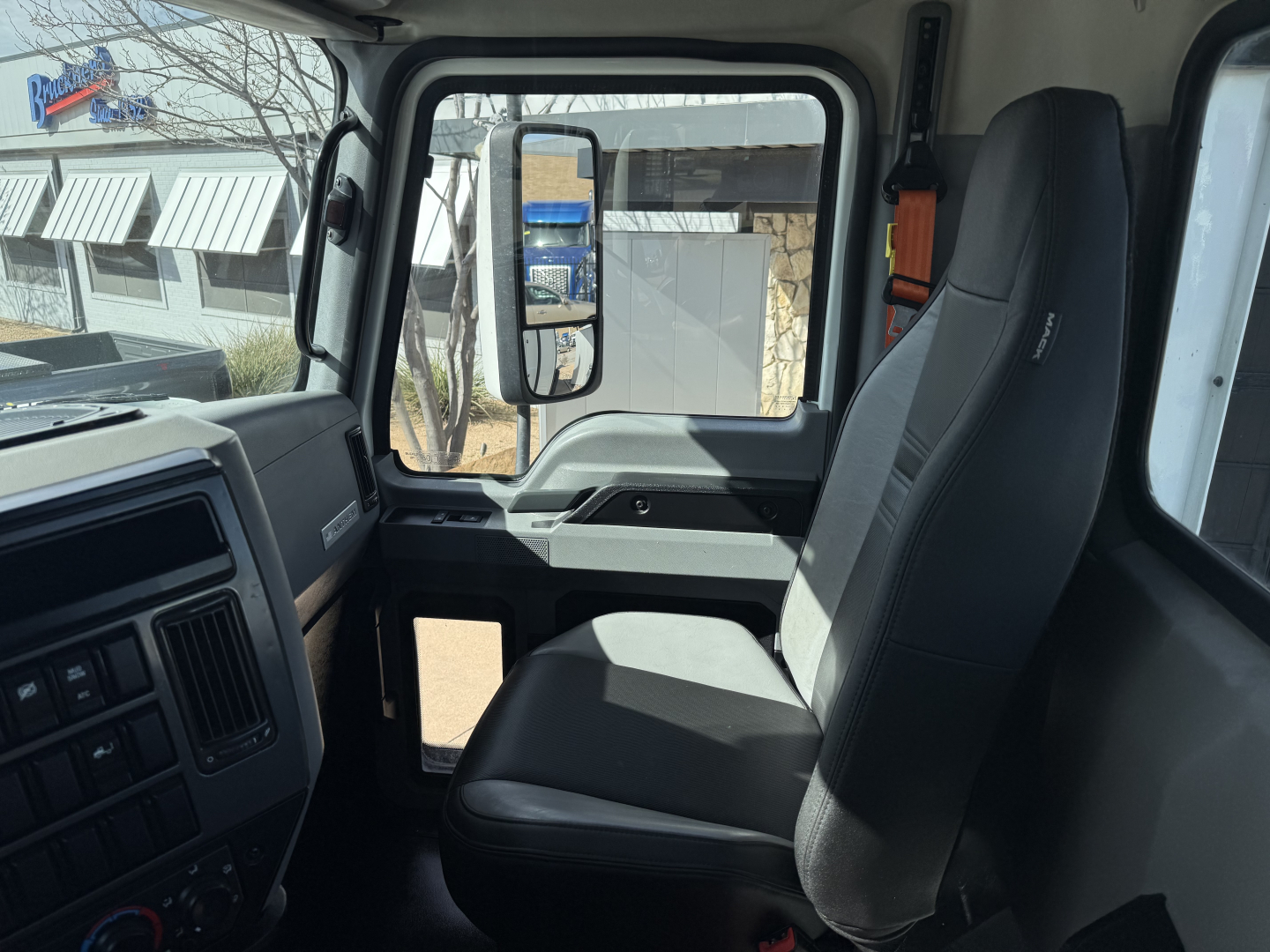 Truck cab interior showing driver seat and dashboard of 2022 Mack AN42T with large side mirror and window glare.