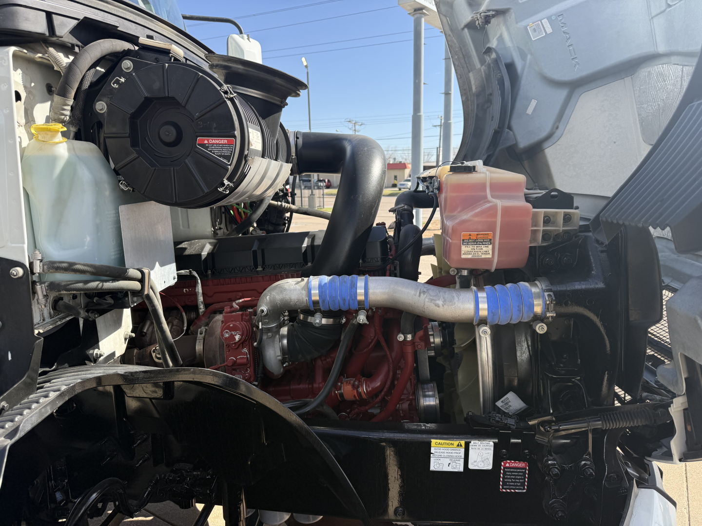 Mack AN42T engine bay showing coolant reservoir, air filter housing, belts, hoses, radiator, and blue silicone couplers attached to a red engine.