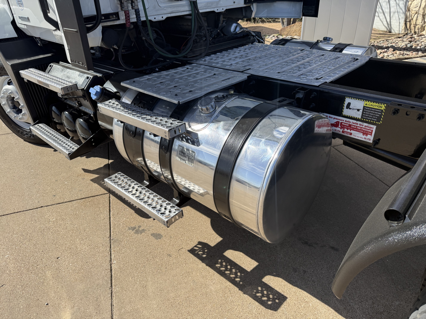 Fuel tank and side steps on a Mack AN42T truck showing chrome cylindrical fuel tank and textured metal steps with surrounding chassis components.