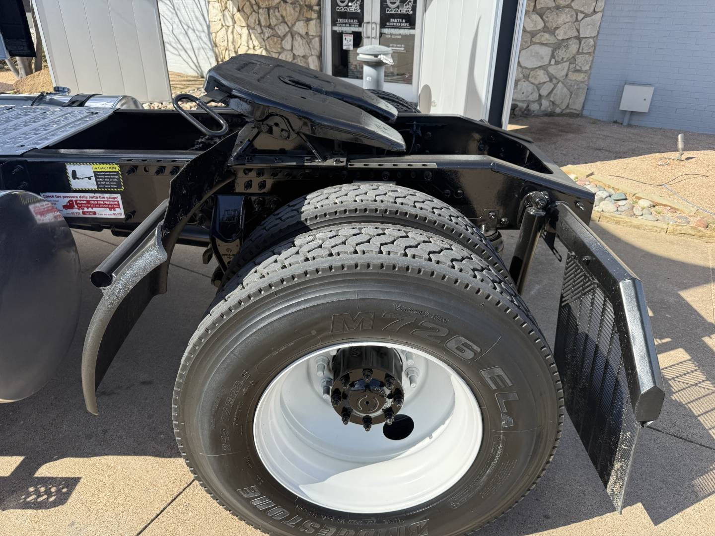 Truck wheel area showing rear chassis and fuel tank, white wheel rim with black tire marked MZZ16E? and visible fender and frame components.