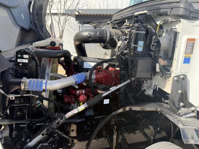 Tractor-trailer engine bay of a 2022 Mack AN42T with red engine block, blue hose, black battery box, and various hoses and components visible.