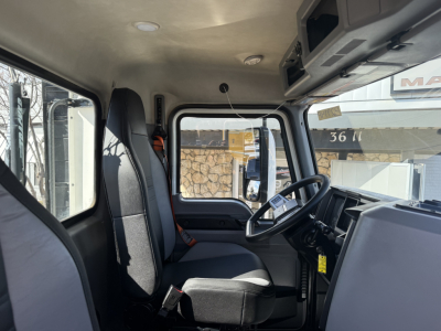 Truck cab interior of 2022 Mack AN42T showing driver seat, steering wheel, dashboard, and front window with overhead storage cabinet.