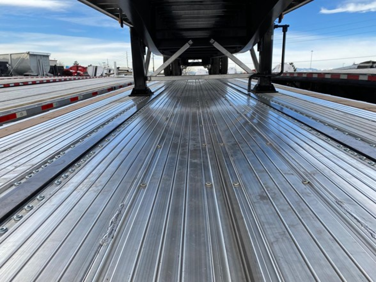 Wide view of a new Utility 4000AE Combo Flatbed trailer showing polished aluminum deck with ribbed surface, side rails, and undercarriage support in the distance.