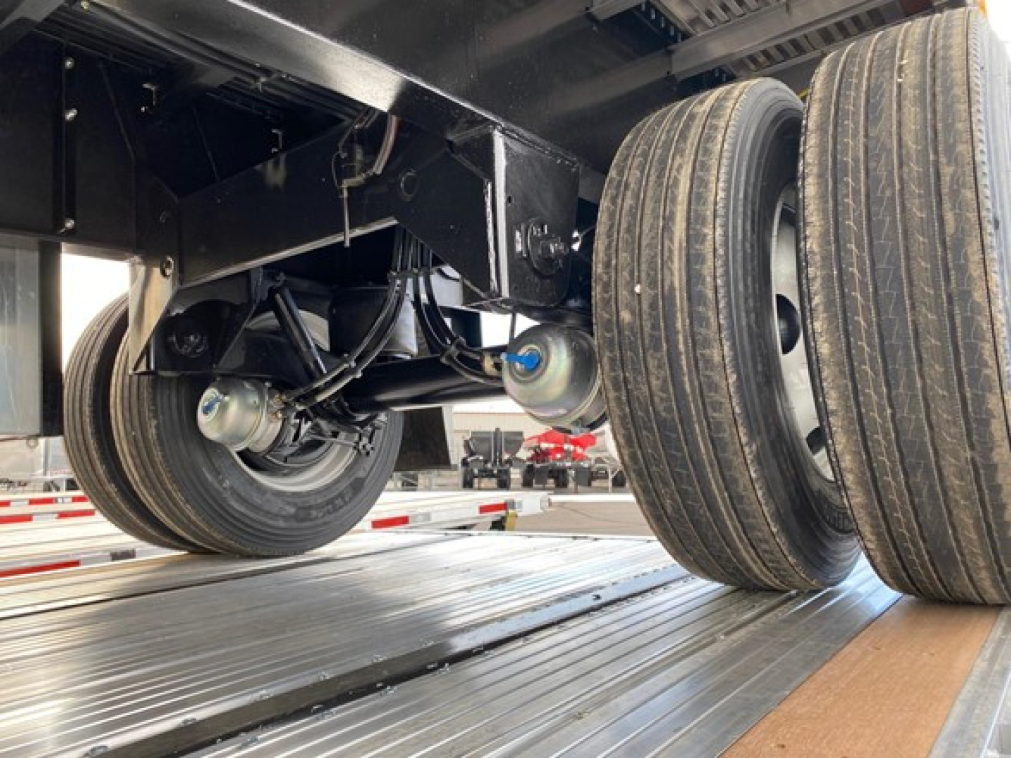 Dual rear axles on a Utility trailer with flatbed and suspension components visible; tires, leaf springs, and undercarriage details in view.