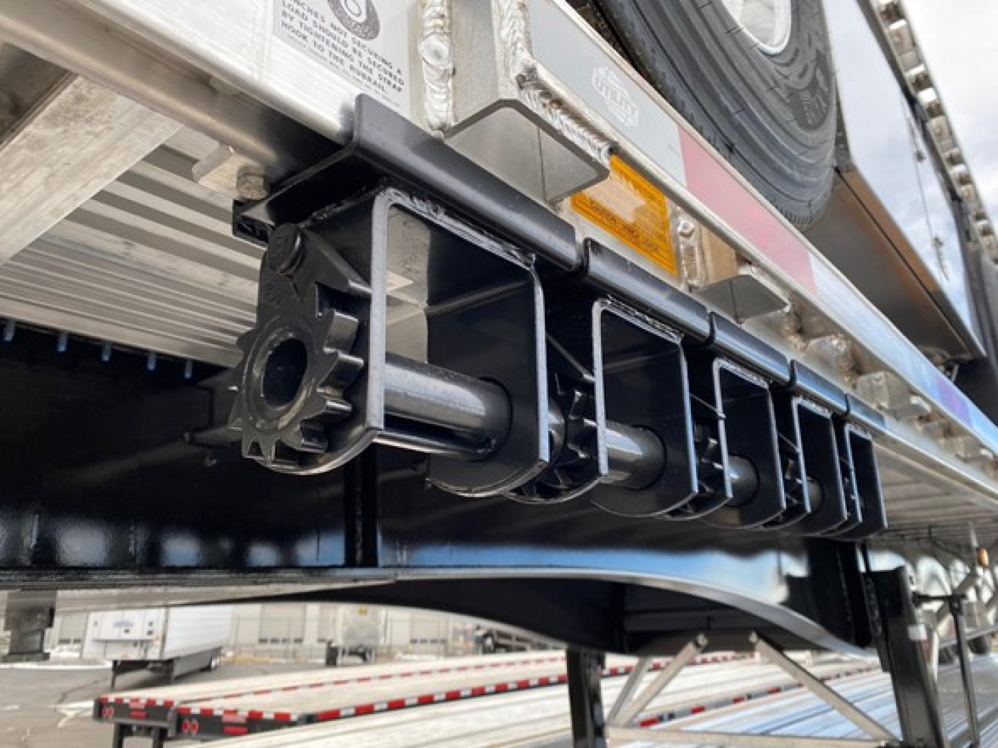 Flatbed trailer undercarriage showing underside assembly and tire on Utility 4000AE combo flatbed with metal frame, warning stickers, and hitch components.