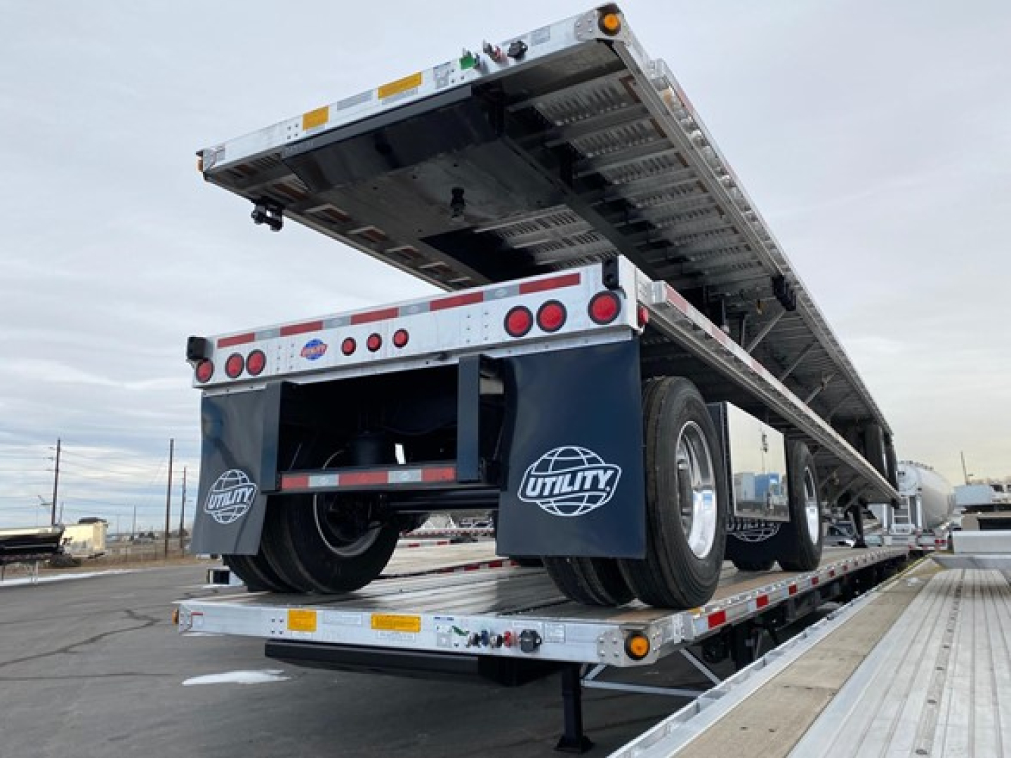 Utility trailer with flatbed deck raised, dual rear wheels, rear lights and mud flaps with Utility logo, on a lowbed trailer transport.