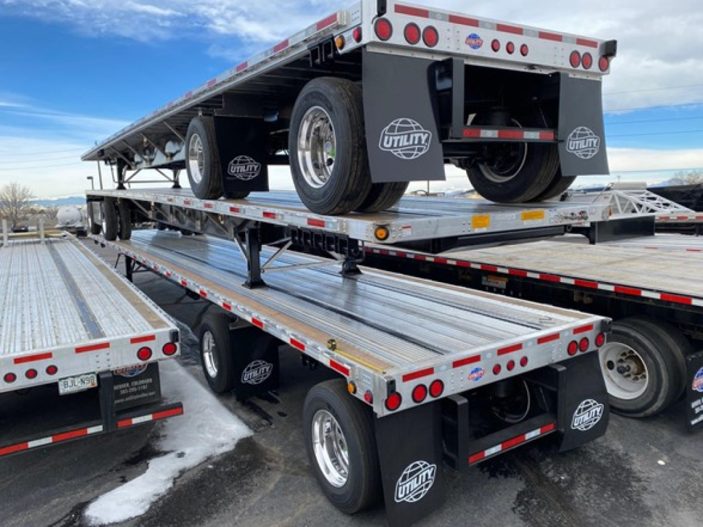 Utility 4000Ae flatbed trailer stack showing dual-axle platform with spare wheel, reflective markers, and Utility logo mudflaps.