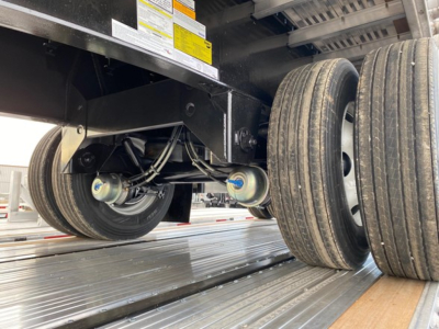 Trailer axle and wheels under a flatbed trailer showing dual rear tires and undercarriage components.
