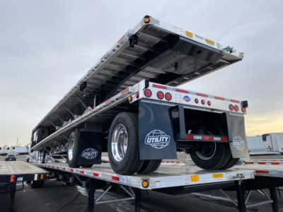Flatbed trailer raised on a loading platform showing rear wheels and mud flaps with Utility logo in a parking lot.
