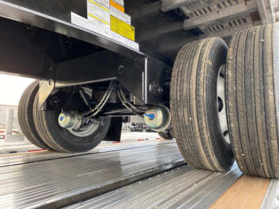 Underbelly of a Utility 4000Ae flatbed trailer showing dual rear axles with pneumatic suspension, leaf springs, wheels, and tires.