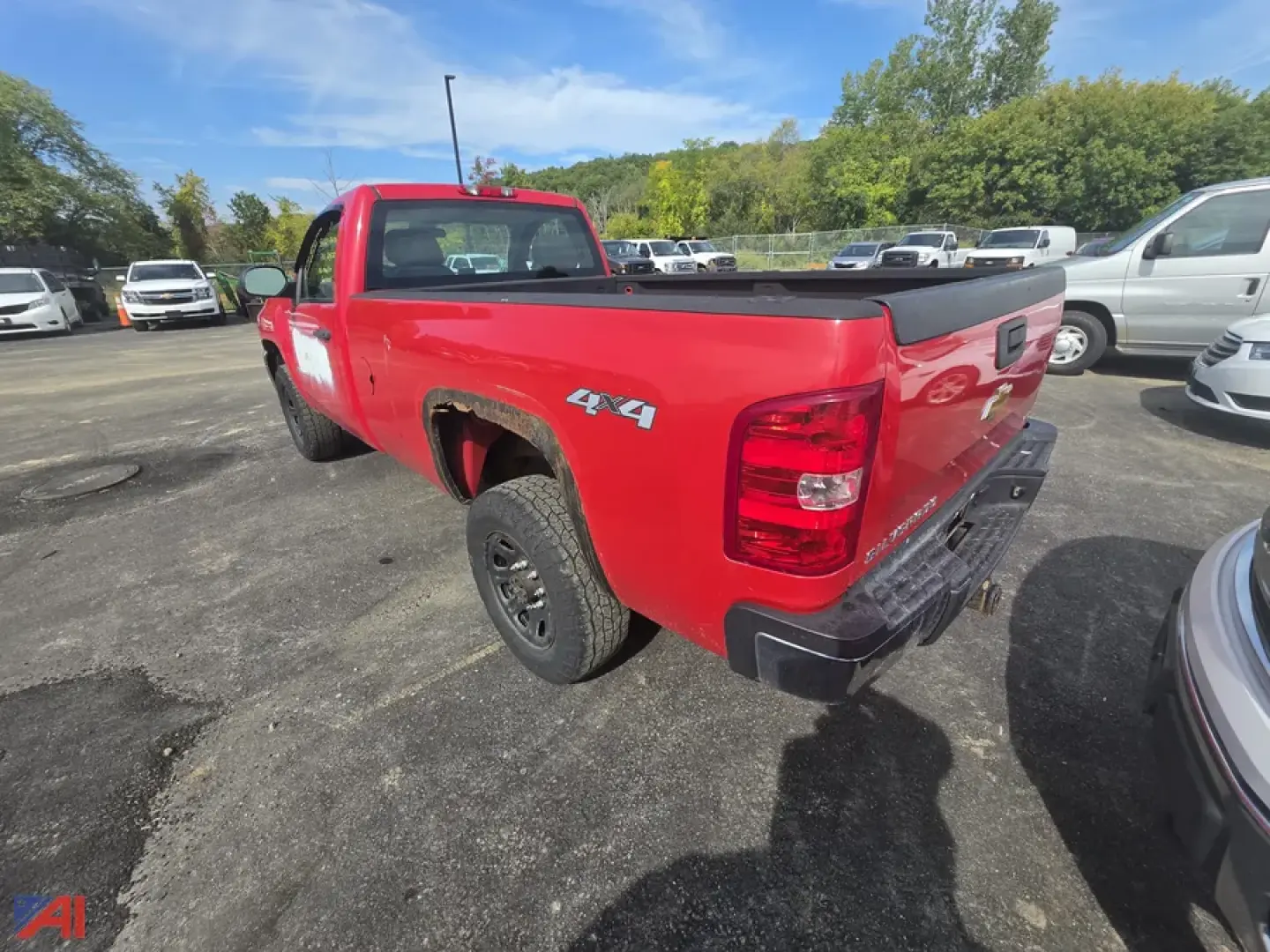 Red Chevrolet Silverado 2500 pickup truck 4x4 with 4x4 decal on rear side, bed cover, in a used vehicle lot. Rear and passenger-side view showing tail light, bumper, and tailgate.