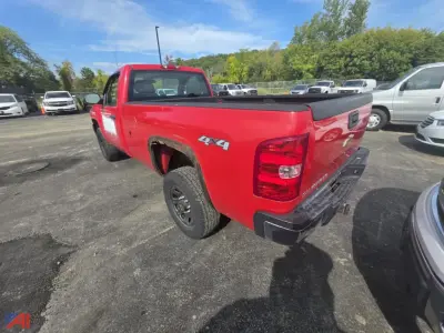 Red Chevrolet Silverado 2500 pickup truck 4x4 with 4x4 decal on rear side, bed cover, in a used vehicle lot. Rear and passenger-side view showing tail light, bumper, and tailgate.