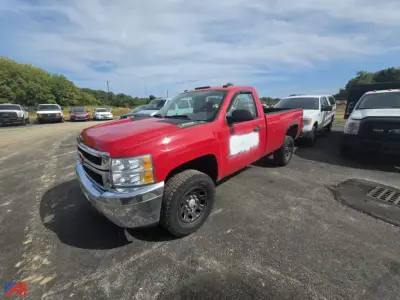 Chevrolet Silverado 2500 pickup truck in red with extended cab, shown in a used-vehicle lot. Front grille and chrome bumper visible; white door sticker faded on side.