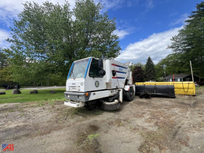 Johnston 3000 sweeper truck in a yard with broom attachments and sweeping equipment visible