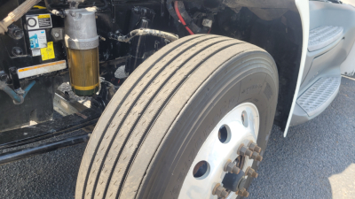 Peterbilt 579 engine bay and front wheel showing front-left tire, suspension components, and shock absorber.