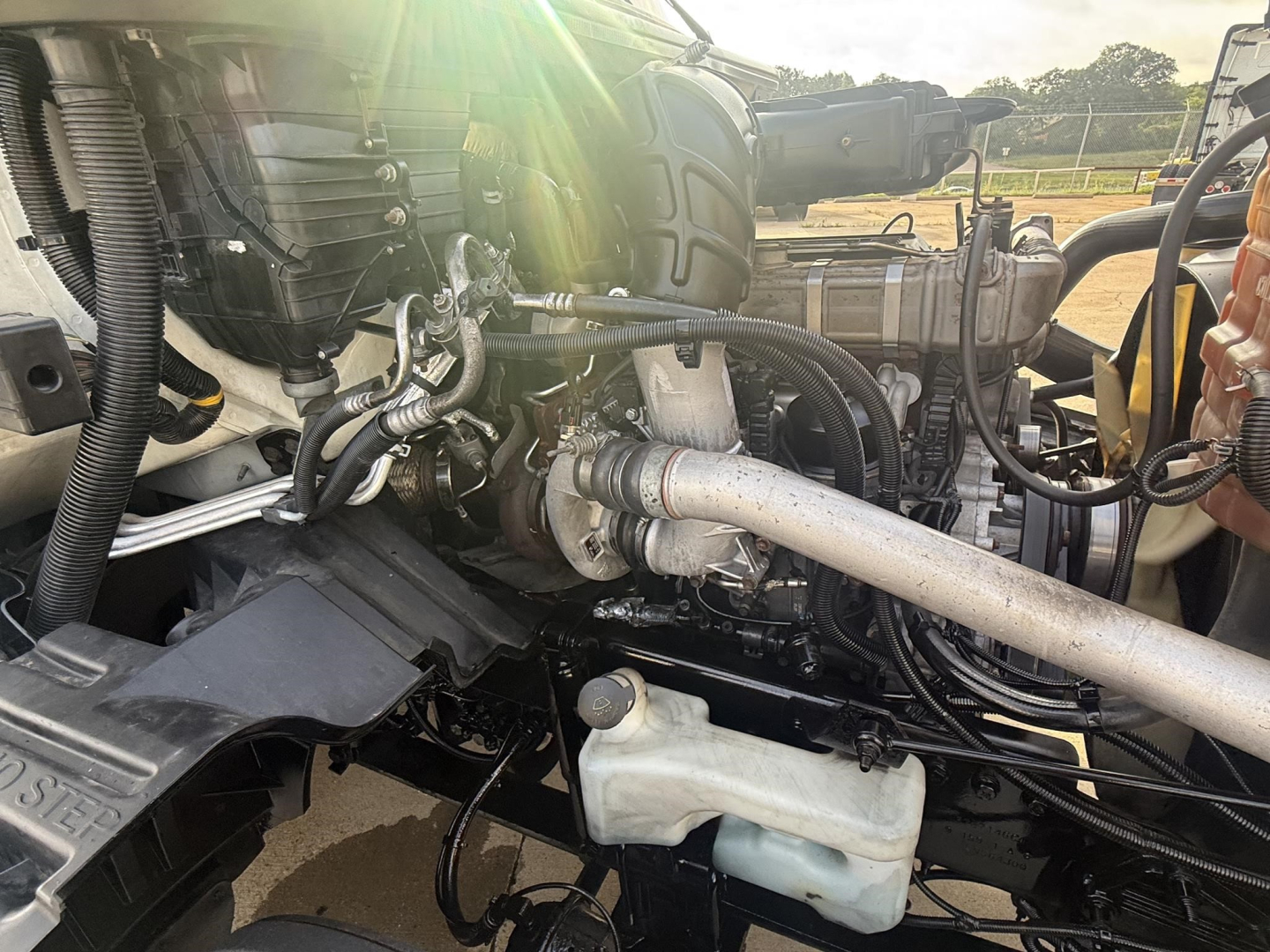 Truck engine bay with exhaust pipe and coolant reservoir visible in a 2020 International LT truck, showing hoses, wiring, and engine components.