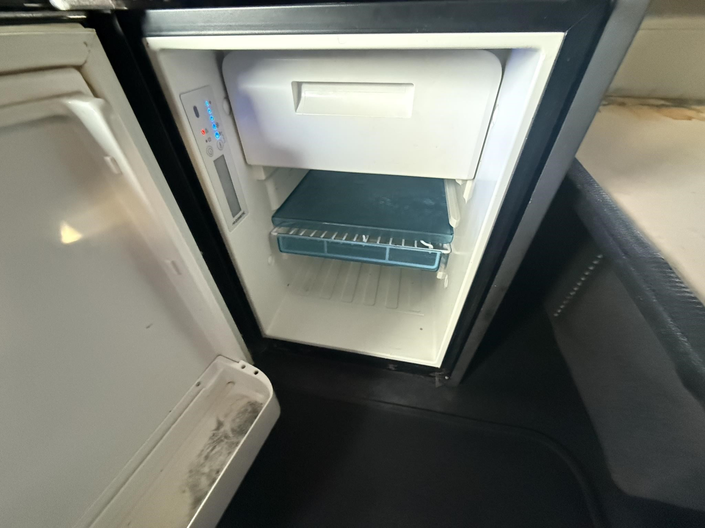 Truck interior showing a compact refrigerator with freezer compartment and a blue restaurant tray on the lower rack.