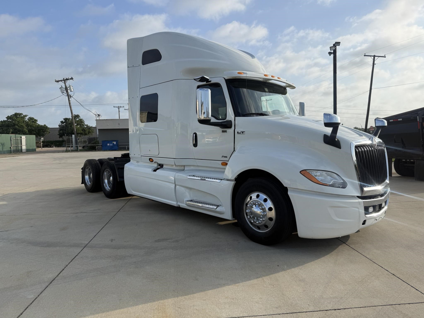 International LT truck in white cab and sleeper, side view showing front grille, headlights, and wheel with 6 tires visible.