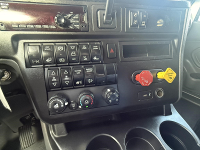 Truck cab dashboard showing controls and gauges in a 2020 International LT sleeper. Visible switches, hazard button, climate knobs, and circular red and yellow knobs; partial radio slot.