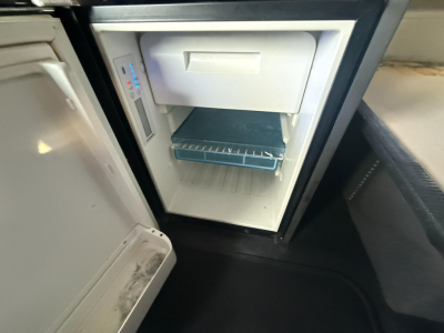 Truck interior showing a compact refrigerator with freezer compartment and a blue restaurant tray on the lower rack.