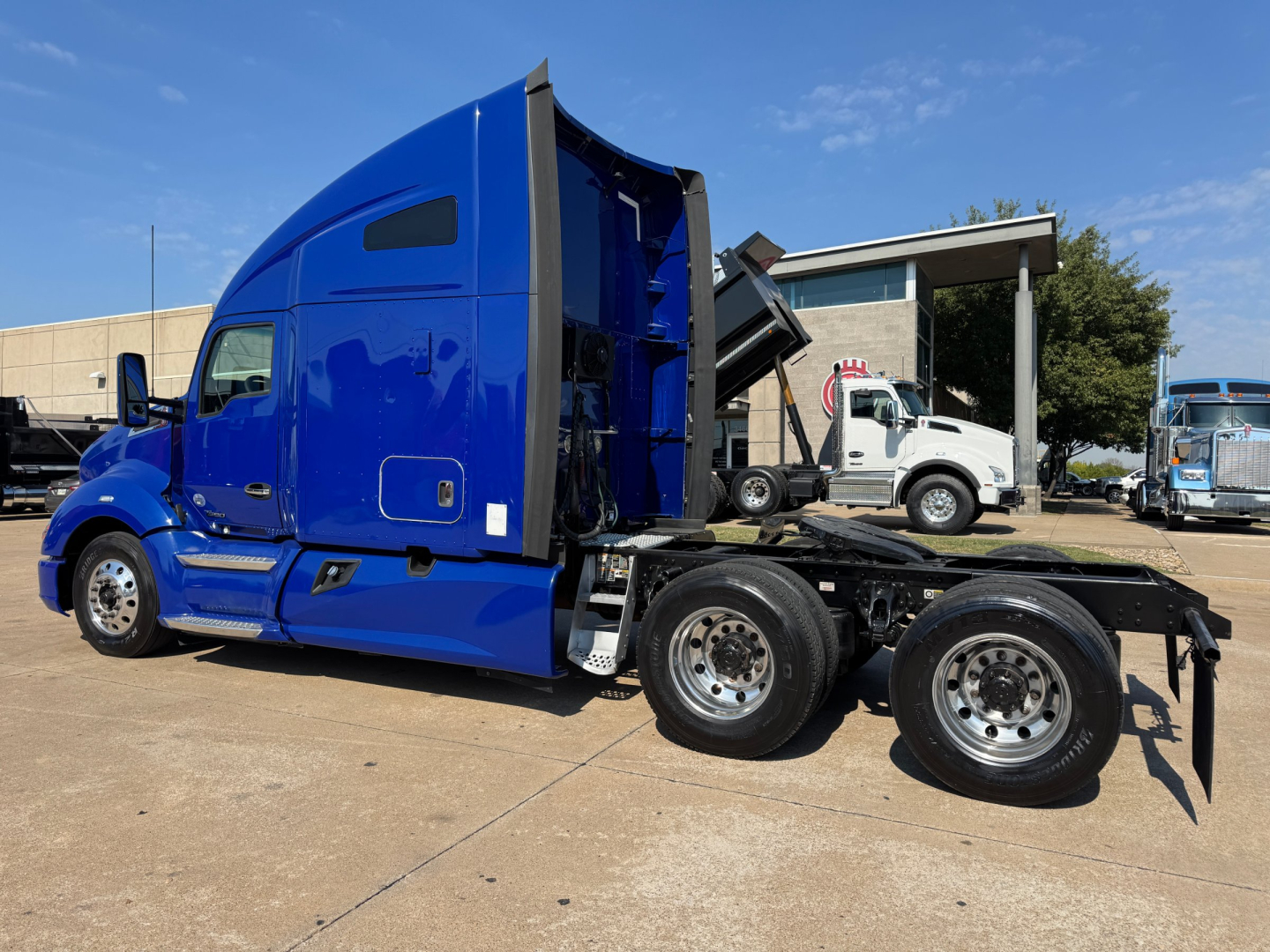 Kenworth T680 truck side view showing blue sleeper cab and rear dump bed/transfer; dual rear axles with chrome wheels; side steps and fuel tanks visible.