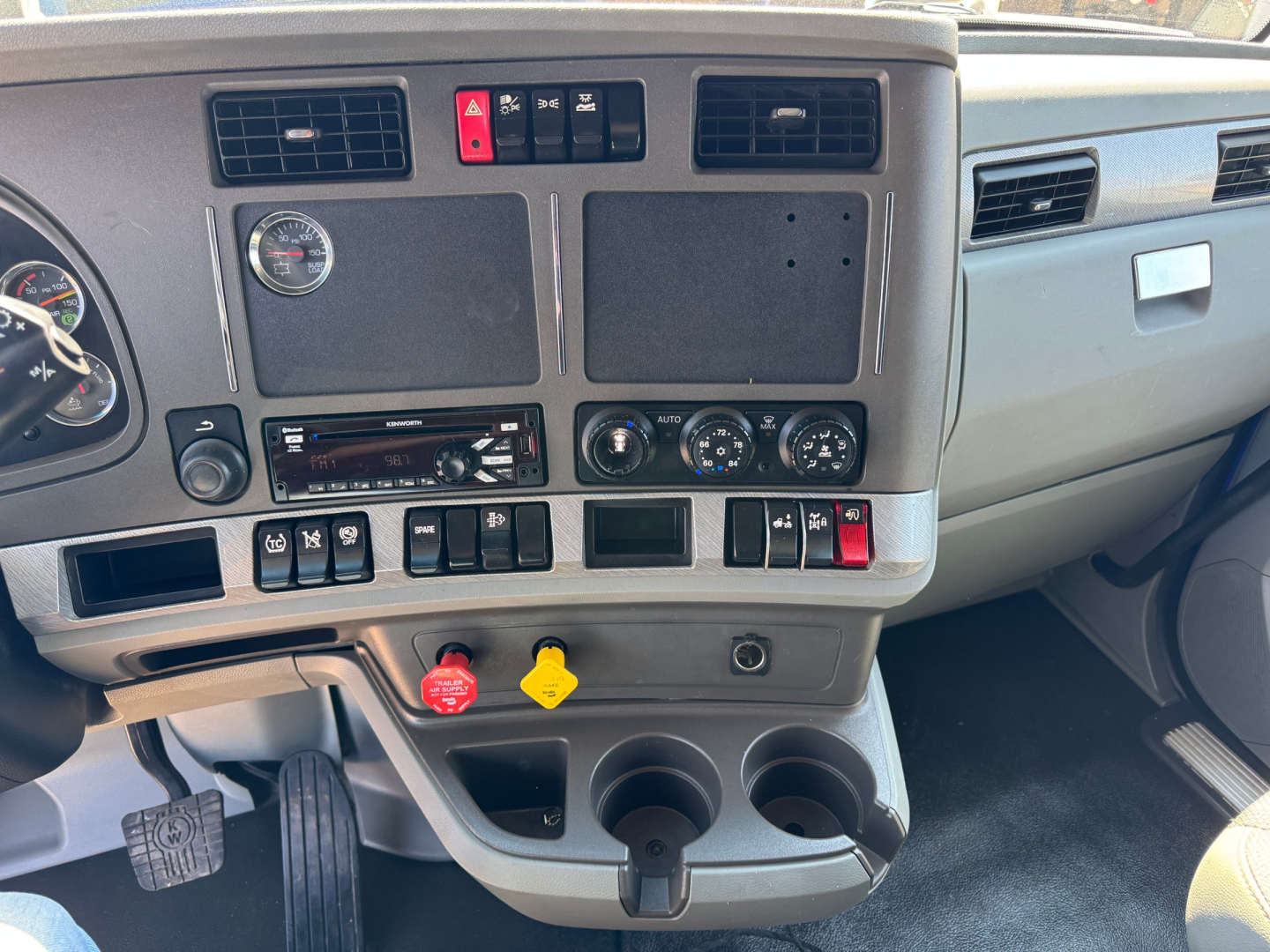 Cabin dashboard of a 2019 Kenworth T680 showing air controls, switches, cup holders, and dashboard gauges.