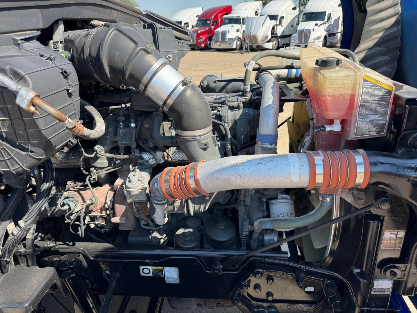 Kenworth T680 engine bay showing air intake hose, coolant reservoir, and various hoses and components.