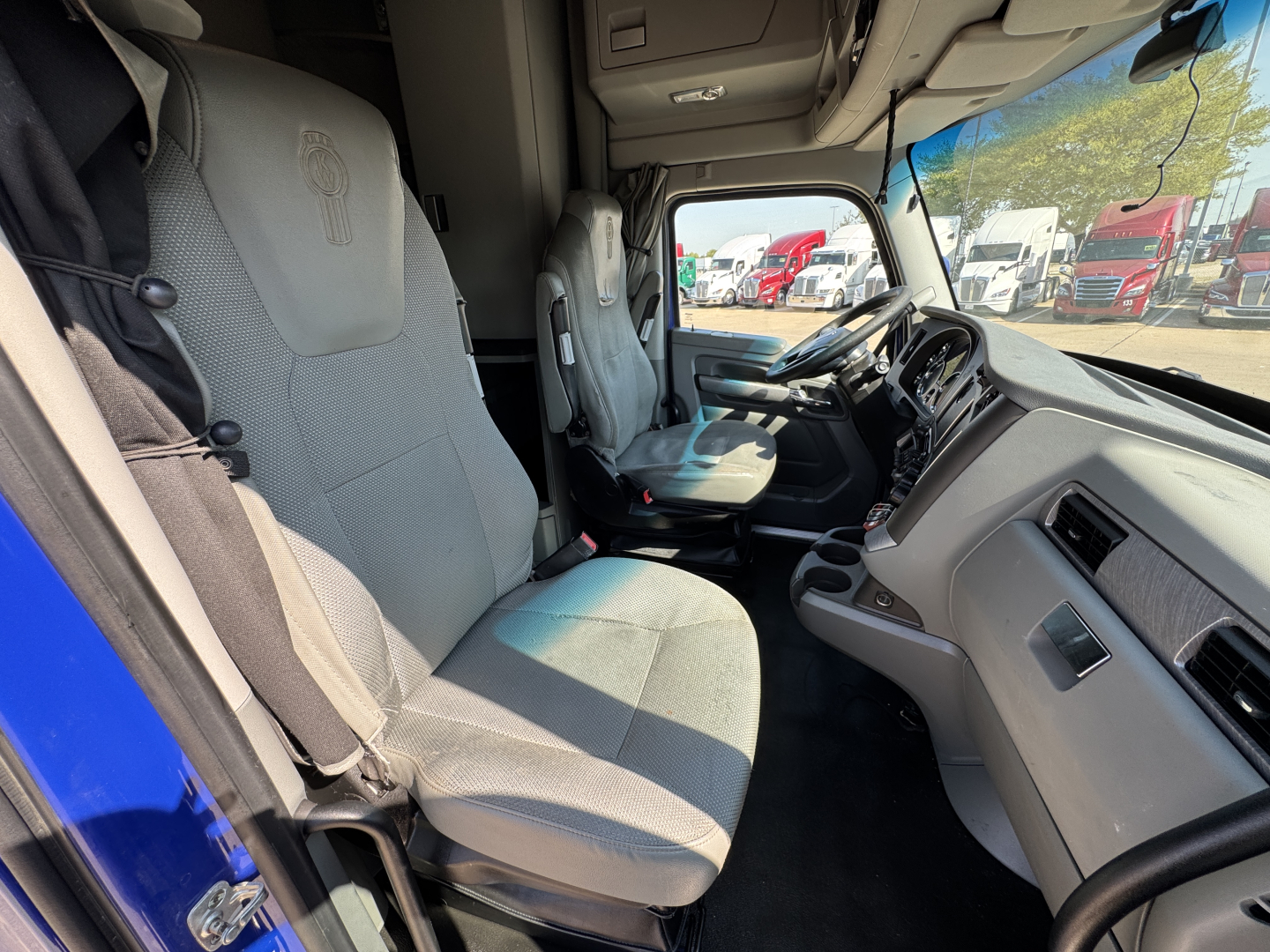 Interior view of a 2019 Kenworth T680 cab showing driver and passenger seats, steering wheel, dashboard, and side window.