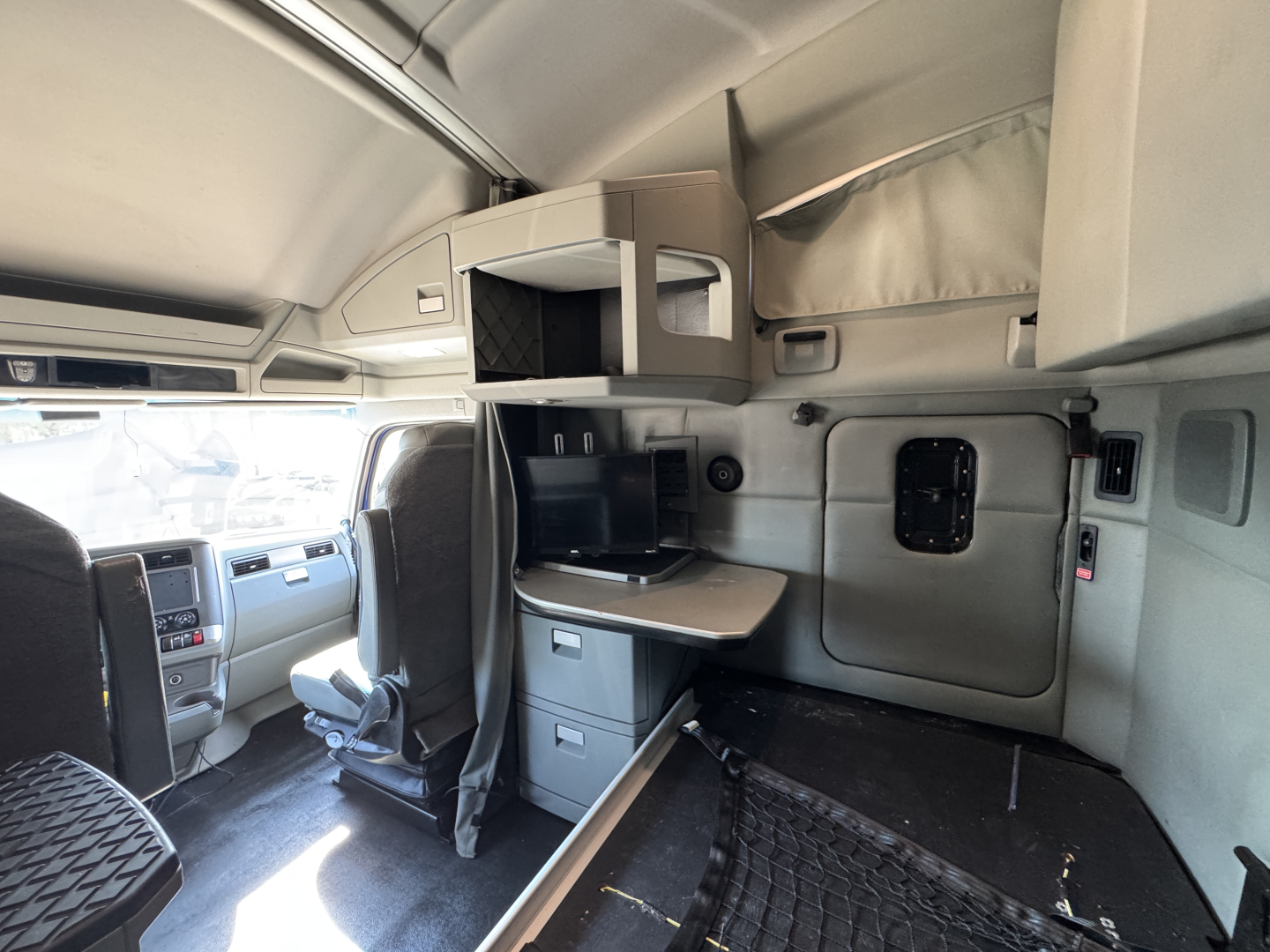 Kenworth T680 sleeper cab interior showing storage shelves, dashboard, and passenger area with overhead compartments.