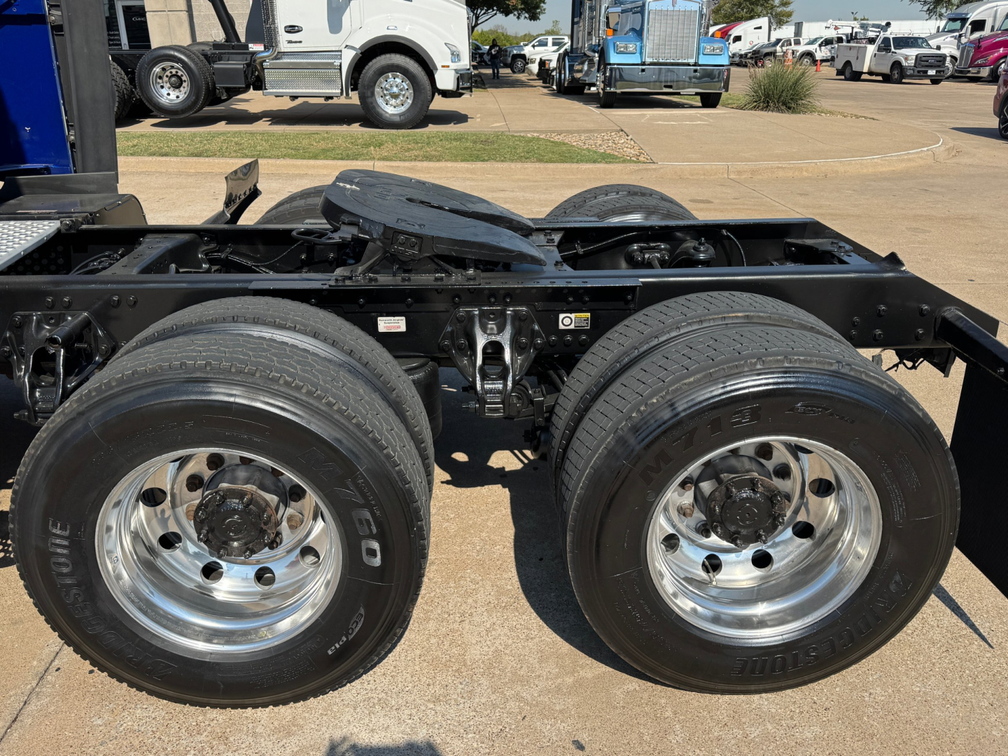 Dual rear axles and frame of a Kenworth truck chassis with chrome wheels and tires visible, no cab attached in this image.