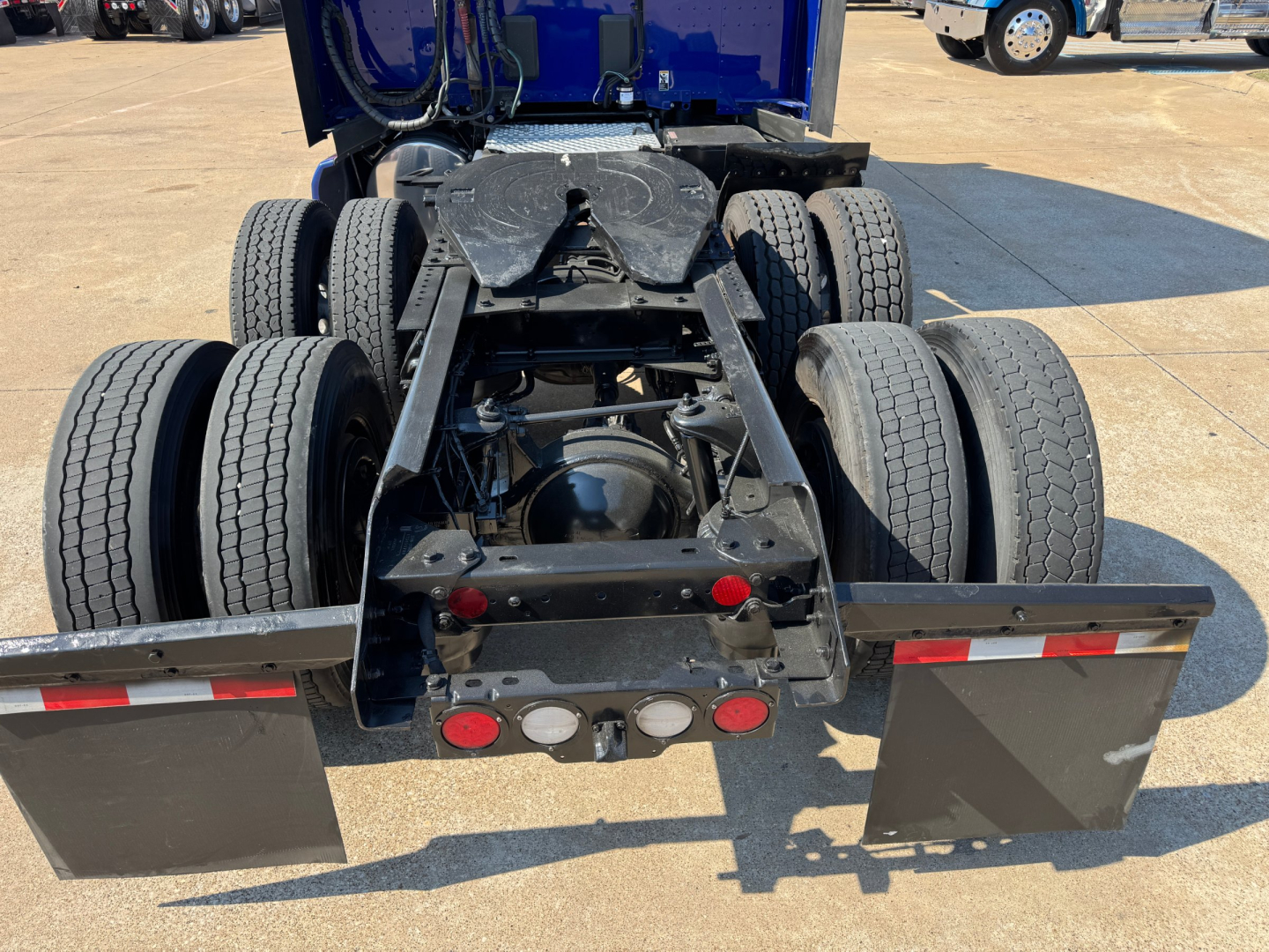 Kenworth T680 rear chassis view showing dual rear axles and fifth-wheel trailer hitch area with brake assemblies and mud flaps.