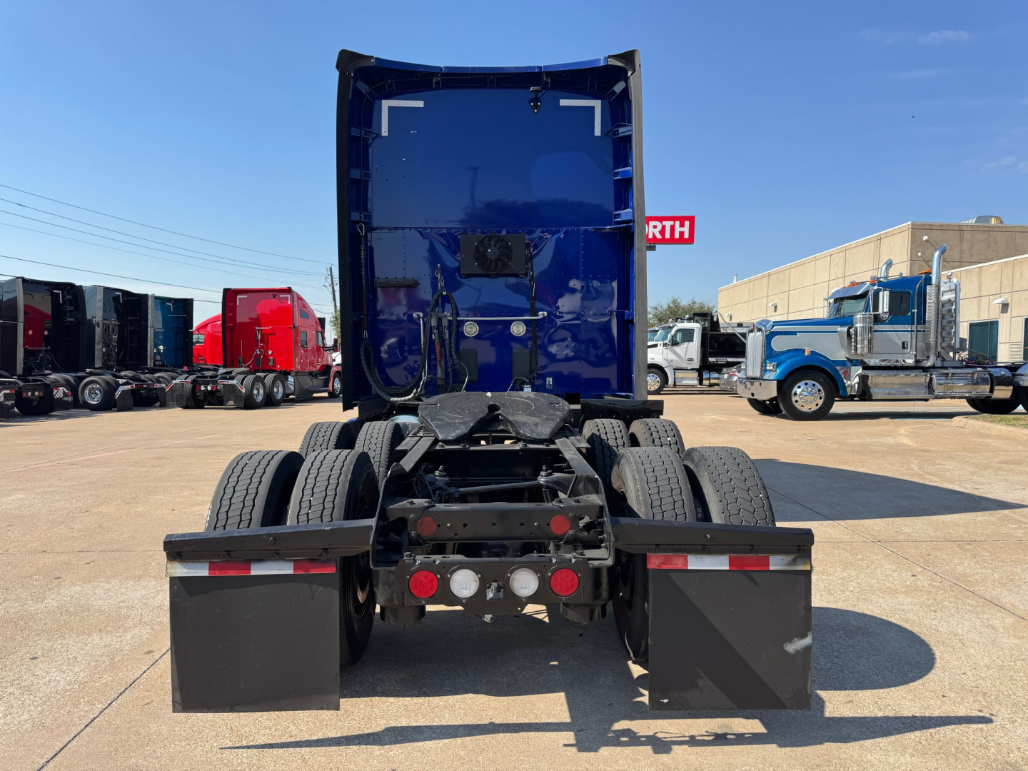 Kenworth T680 chassis rear view showing fifth wheel and dual fuel tanks with mudflaps and rear lights.